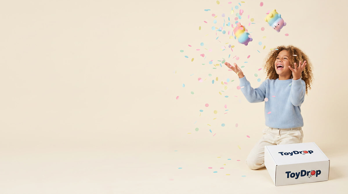 Girl kneeling beside a white ToyDrop box tossing pastel squishies and confetti into the air