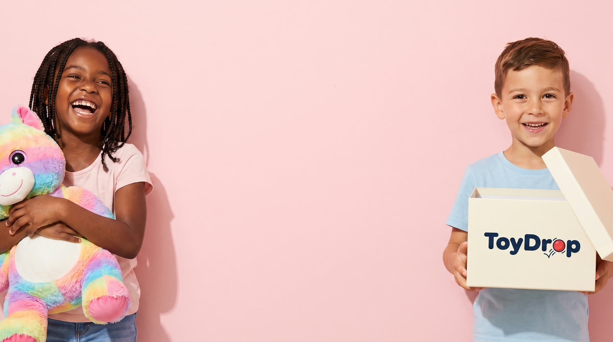 Girl holding a rainbow unicorn plush and boy holding a white ToyDrop box on a pink background