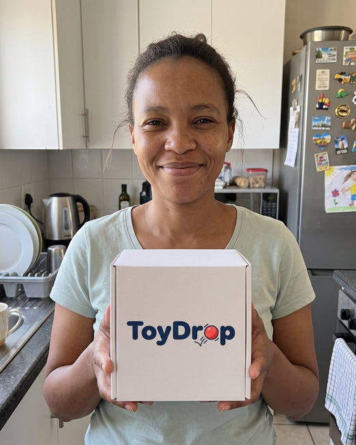 Smiling woman in her kitchen holding a white ToyDrop box