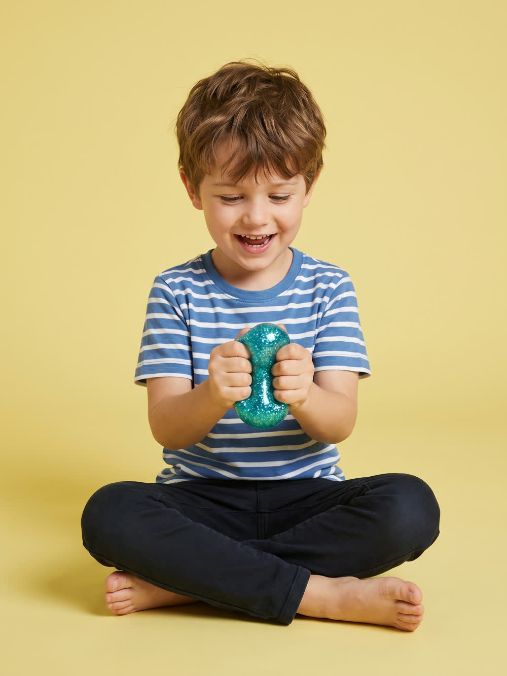 Boy stretching a teal glitter squishy between both hands on a yellow studio background