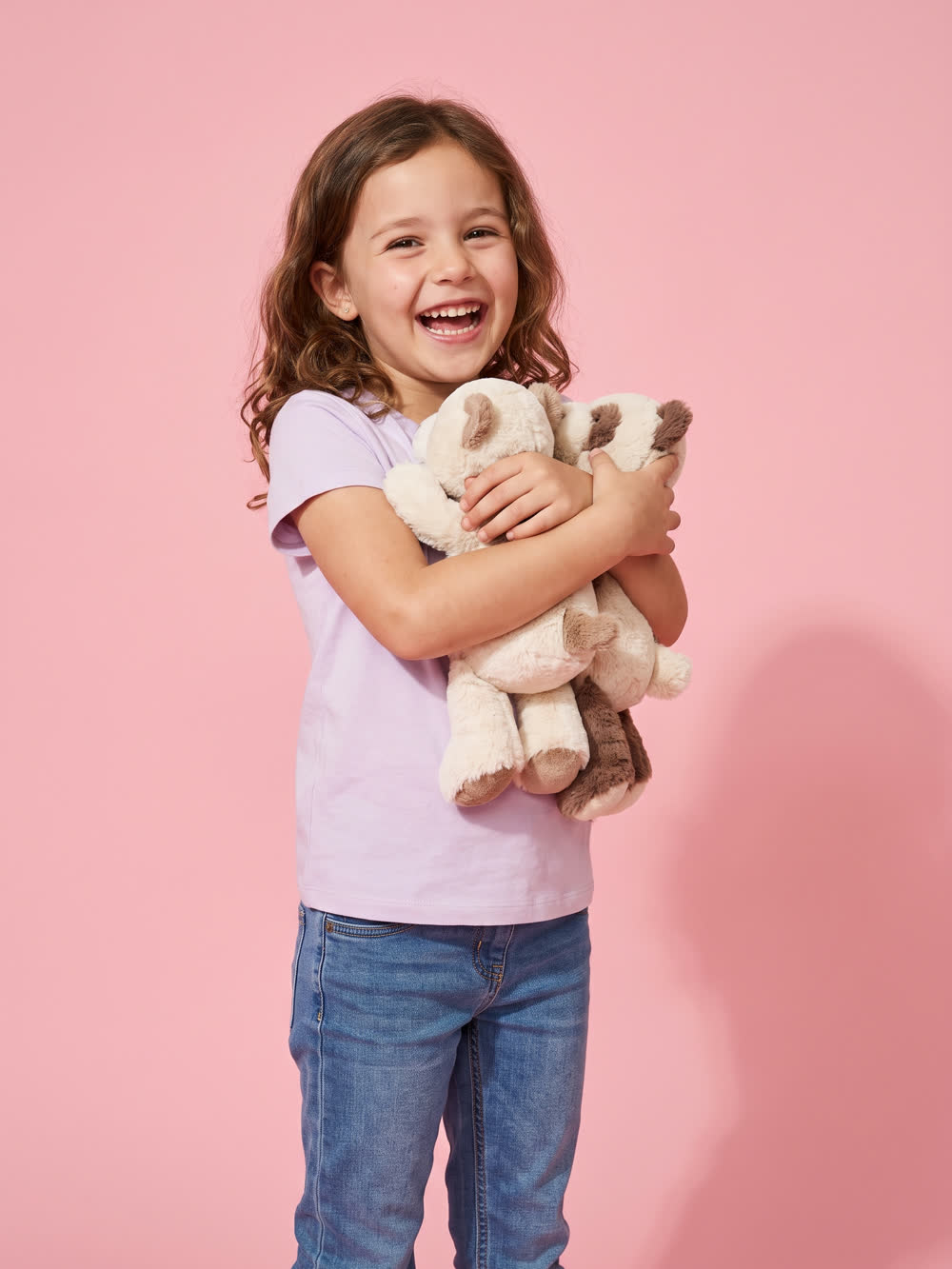 Girl in a lilac t-shirt hugging two soft teddies on a pink studio background